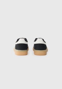 Black and white sneakers with a suede upper, round toe, rubber sole, and contrasting gum rubber outsole. Laced closure at the back.