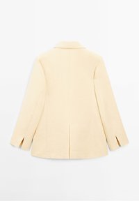 Jasnożółta marynarka wykonana z gładkiej tkaniny, z wyciętym kołnierzem, długimi rękawami i rozcięciem z tyłu.