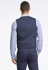 Marineblauer Weste mit strukturierter Oberfläche, getragen über einem hellblauen und weißen gestreiften Hemd. Glatter Stoff, taillierte Passform, keine sichtbaren Verzierungen.