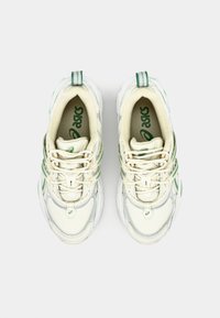 Baskets blanches avec accents verts, en matériaux en mesh et synthétiques, à bout rond, avec un collier rembourré et un design à lacets.