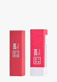 Czerwona szminka w matowej tubce; kwadratowy design z białym tekstem. Zawiera błyszczące różowo-białe pudełko z podobnymi detalami marki.