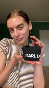 Black fabric mini bag with a top handle, featuring a prominent white "KARL LA" logo. Compact design with zipper closure and silver hardware accents.