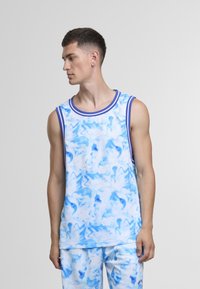 Ung mann med kort mørkt hår iført en blå og hvit sports-topp uten ermer med abstrakt mønster og matchende shorts, som ser mot venstre.