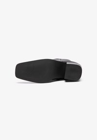 Suela de zapato negra con un acabado mate y suave. Presenta una forma redondeada y un sutil patrón texturizado para mayor agarre. Diseño plano sin acentos prominentes.
