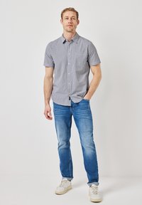 Kortärmad rutmönstrad skjorta i marinblått och vitt, med knappframsidan och en bröstficka, i kombination med ljusblå jeans och vita sneakers.