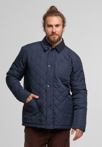 Marineblauer gesteppter Blouson mit Cordkragen, Druckknöpfen und einer Brusttasche, seitlichen Taschen und einem strukturierten Material.