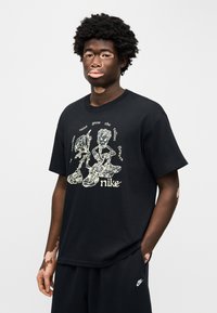 Μαύρο βαμβακερό T-shirt με γραφική εκτύπωση καρικατουριστικών φιγούρων και κειμένου, κοντά μανίκια και χαλαρή εφαρμογή. Συνδυάζεται με μαύρο σορτς.