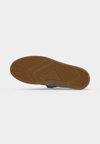 Semelle en caoutchouc marron d’une chaussure avec des motifs géométriques texturés et une petite partie perforée au centre.
