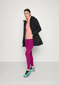 Juodas gobtuvas paltas, rožinė aukšta kaklo palaidinė, ryškiai rožinės spalvos legginsai ir mėlynai juodi sportbačiai. Lygi tekstūra; modernaus, siauro silueto dizainas.