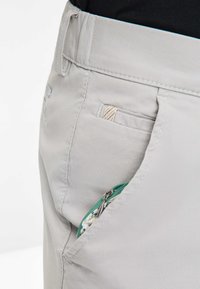 Light gray pants with a textured finish, featuring a zippered pocket with a green zipper and a decorative inner lining.