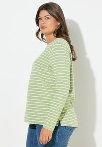 Šedé tričko s dlouhým rukávem s neonově zelenými horizontálními pruhy. Má výstřih do lodi a volný střih, v kombinaci s modrými džínami.