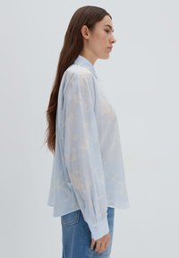 Blusa leggera azzurra, trasparente, con colletto classico, maniche lunghe e delicati motivi astratti. Polsini con bottoni e vestibilità rilassata.