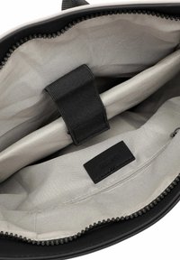 Musta koti sisu, kus on sile beež vooder, must kangast jagaja ja nahk silt, millel on embosseeritud tekst. Näha on lukuga detail.