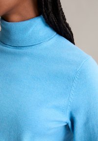 Lichtblauwe coltrui gemaakt van zacht materiaal, met een geribbelde kraag en een gladde textuur in een aansluitende pasvorm.