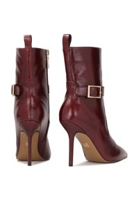 Stivali alla caviglia in pelle color bordeaux con punta affusolata, tacco alto a stiletto e zip laterale. Presentano un accento a cintura con un dettaglio in fibbia dorata.