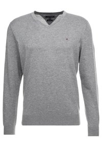 Suéter gris de cuello en v hecho de una suave tela de punto. Mangas largas, puños y dobladillo acanalados, con un pequeño logo en el pecho.
