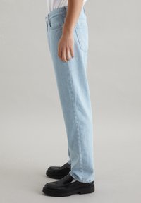 Jeans de mezclilla azul claro con un diseño de pierna recta. Presentan una cinturilla con un cierre de botón y bolsillos laterales. Llevados con mocasines negros.