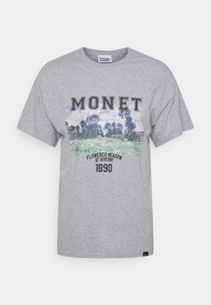 T-shirt grigia con la scritta "MONET", un paesaggio dipinto di un prato fiorito e la scritta "Flowered Meadow at Giverny 1890" stampata sotto.
