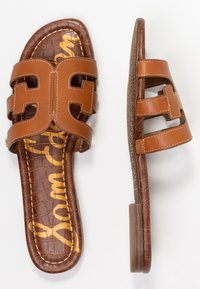 Sandalia de cuero marrón tipo slide con doble tirante y diseño troquelado, suela marrón texturizada y plantilla con patrón y letras doradas.