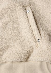 Crème-kleurige fleece trui met een gestructureerde, fluffy oppervlakte en ribgebreide accenten bij de mouwen en onderkant; heeft een zilveren drukknoop_detail.