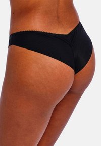 String noir en coton avec une texture douce, présentant un bord délicat en scallop et un design taille basse qui met en valeur la silhouette de la taille.