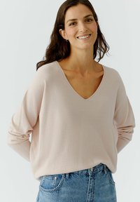 Helles rosa, langärmliges Pullover-Sweatshirt mit V-Ausschnitt in Ripptextur, kombiniert mit blauen Jeans. Weicher Stoff mit lockerer Passform.