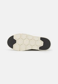 Rubber shoe sole with a textured honeycomb pattern. Predominantly cream with a black accent on the toe area.