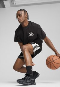 Sort t-shirt med et hvidt grafik. Sorte og hvide mønstrede shorts. Sorte atletiske sko med tekstureret detaljering. Orange basketball.