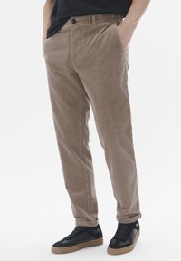 Tan corduroy trousers with a relaxed fit, featuring side pockets and a button closure, paired with black low-top sneakers.
