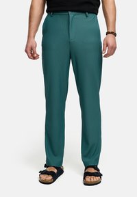Teal farvede, ribbede bukser med lige ben, der har lynlåsgylp og knaplukning samt sidelommer. Bæres med sorte sandaler.