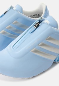 Ανοιχτό μπλε sneakers χωρίς κορδόνια με φερμουάρ μπροστά, τρεις ασημένιες ρίγες στα πλαϊνά και λευκή εσωτερική επένδυση, με την ετικέτα "MEGARIDE 92".
