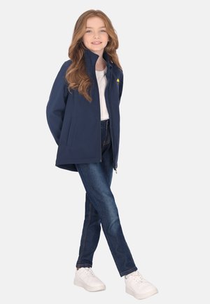 Marinejakke med høj krave og sidelommer, parret med blå jeans og hvide sneakers, med et lille gult paraplylogo.