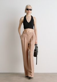 Svart cropped halterneck-top kombinert med beige vide bukser med frontfold. Tilbehør inkludert en liten svart håndveske og solbriller.