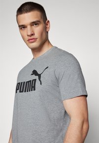 Grå bomulds t-shirt med et stort sort "PUMA" logo og en silhuet af en pumabar. Kortærmet med rund halsudskæring.