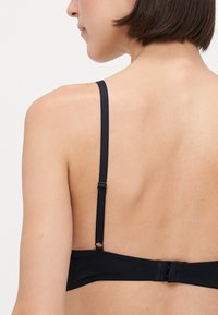 Black bra with adjustable straps and hook-and-eye closure. Smooth fabric texture with minimalistic design, seen from the back.