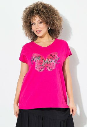 Camiseta rosa con escote en V, con un gráfico de mariposa en rosa y negro y el texto "espíritu libre" en cursiva. Mangas cortas, corte relajado.
