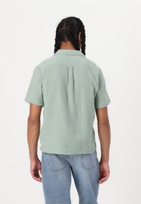 Korte mouwen, mintgroen shirt van gestructureerde stof. Beschikt over een rugpand en een rechte zoom, gecombineerd met lichtblauwe jeans.