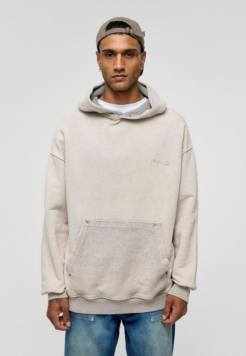 Crèmekleurige hoodie met een contrasterende gestructureerde zak, geribde zoom en manchetten. Het heeft een gelaagde uitstraling met een grijze halslijn.