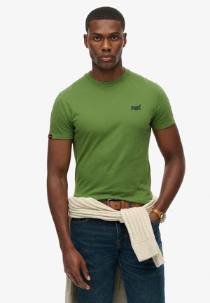 Green cotton t-shirt with short sleeves and a round neckline, featuring a dark blue logo on the chest and a textured cream sweater tied at the waist.