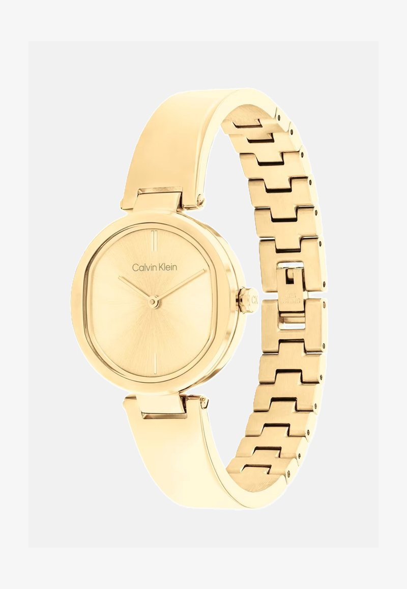 Kuldne Calvin Kleini kell, millel on ümmargune, päikesepaistega kelladial ja seotud metallist käevõru, poleeritud viimistluse ja minimalistlike aktsentidega.