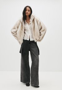 Kremowa pikowana kurtka z sztucznego futra w oversize, połączona z białą koszulą z guzikami oraz szerokimi czarnymi dżinsami, z kontrastowym przeszyciem.