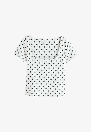 Baltas trumpomis rankovėmis nukirptas viršus su kvadrato formos iškirpte, puoštas juodu polka taškų raštu, tolygiai pasiskirsčiusiu ant audinio.