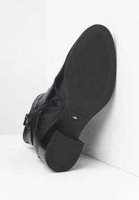 Bottine en cuir noir avec un talon bas, dotée d'une fermeture éclair et d'une semelle en caoutchouc texturé. Fabriquée en Italie avec un logo sur le côté.