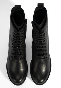 Zwarte leren enkelboots hebben een gestructureerd oppervlak, een ronde neus, veterbinding aan de voorkant en een zijrits voor gemakkelijk aan- en uittrekken.