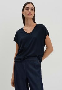 T-shirt a V in velluto blu navy con maniche corte, realizzato in tessuto morbido. Presenta una vestibilità rilassata e cade leggermente in vita. Abbinato a un denim scuro.