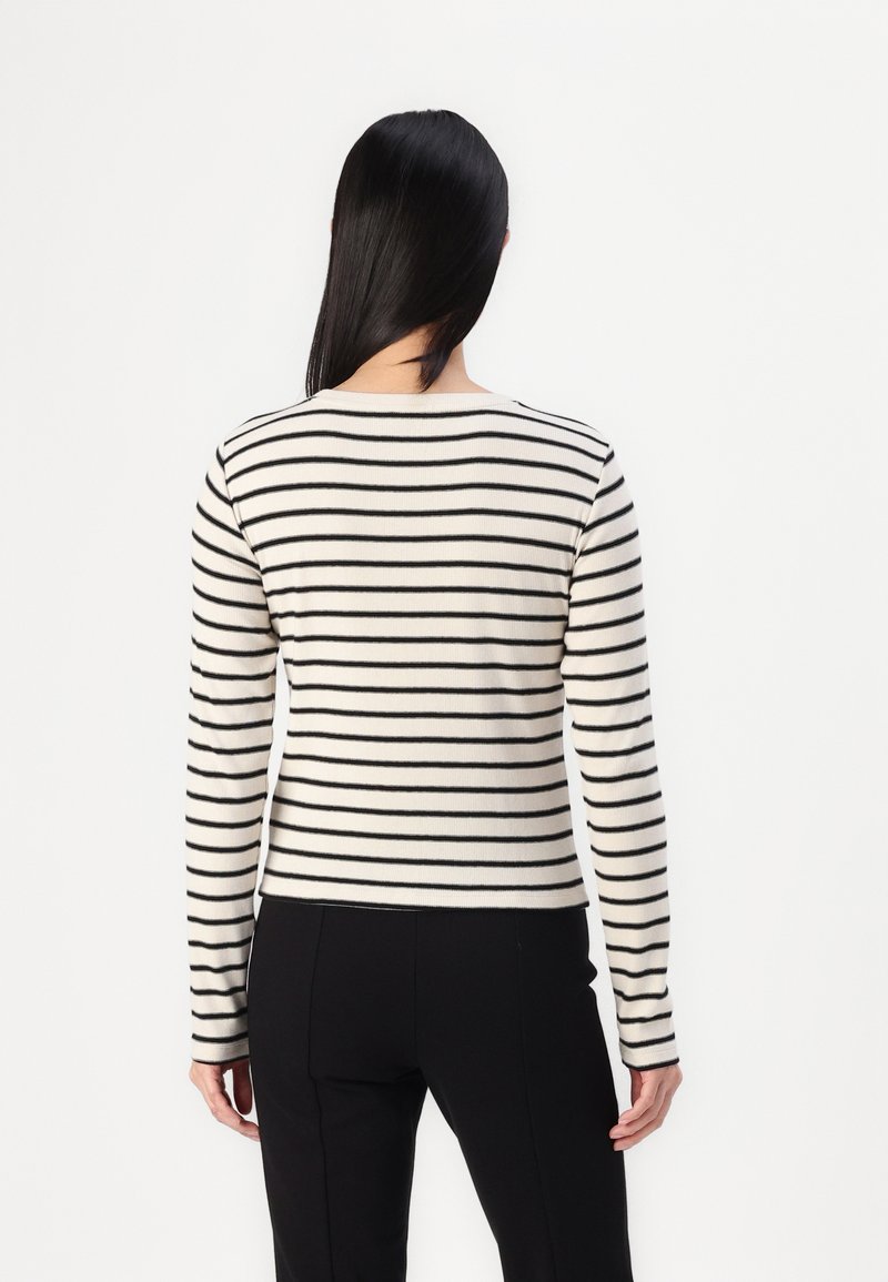 Pull en rayures noir et blanc avec des manches longues, un col rond et une coupe ajustée. Texture tricotée avec une finition lisse.