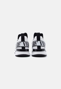 Λευκά αθλητικά παπούτσια με μαύρες λεπτομέρειες, που διαθέτουν πλέγμα στο πάνω μέρος, επενδυμένο κολάρο και εμφανές ιμάντα με το λογότυπο στη φτέρνα.