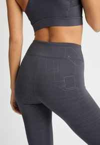 Leggings atléticos grises con una cintura alta, que presentan un patrón geométrico y una textura suave. Hechas de un material elástico que absorbe la humedad.