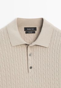 Beige poloshirt met korte mouwen, kabelbreipatroon, twee grijze knopen en een "Massimo Dutti" label aan de binnenkant van de kraag.