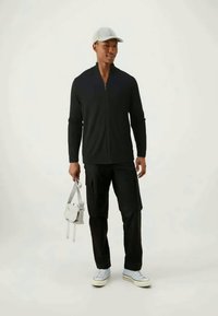 Giacca nera con zip, pantaloni cargo neri e sneakers azzurro chiaro. Cappello grigio e borsa grigia chiara con cinghie. Design semplice, vestibilità comoda.